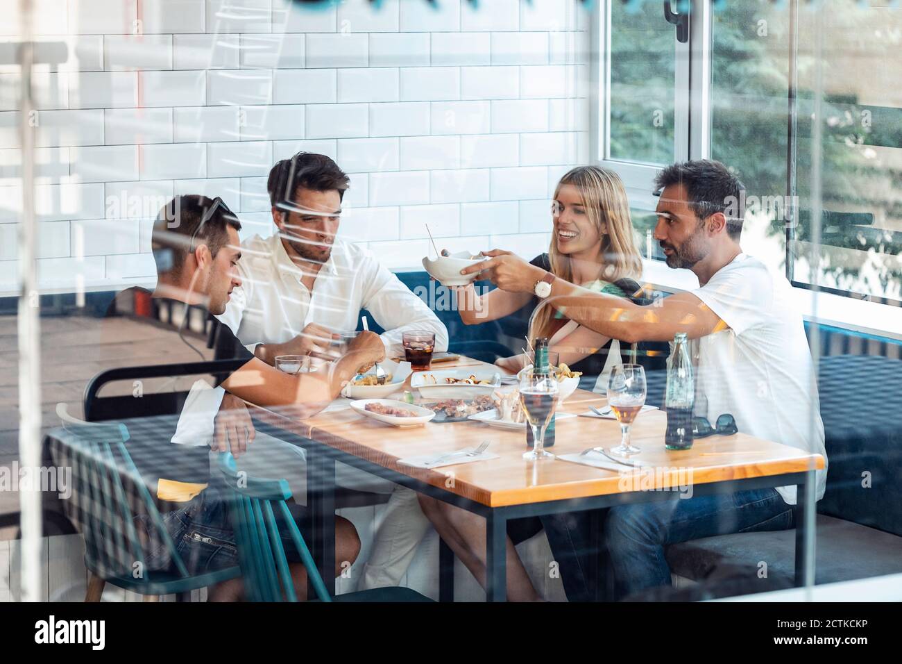 Friends enjoying meal at restaurant seen through window Stock Photo