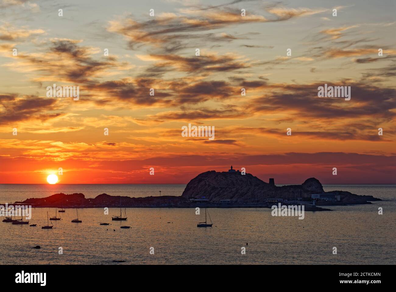 France, Haute-Corse, LIle-Rousse, Silhouettes of sailboats in front of small Mediterranean island at moody sunset Stock Photo