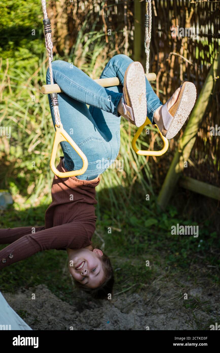 Girl hanging upside down on rod in backyard Stock Photo