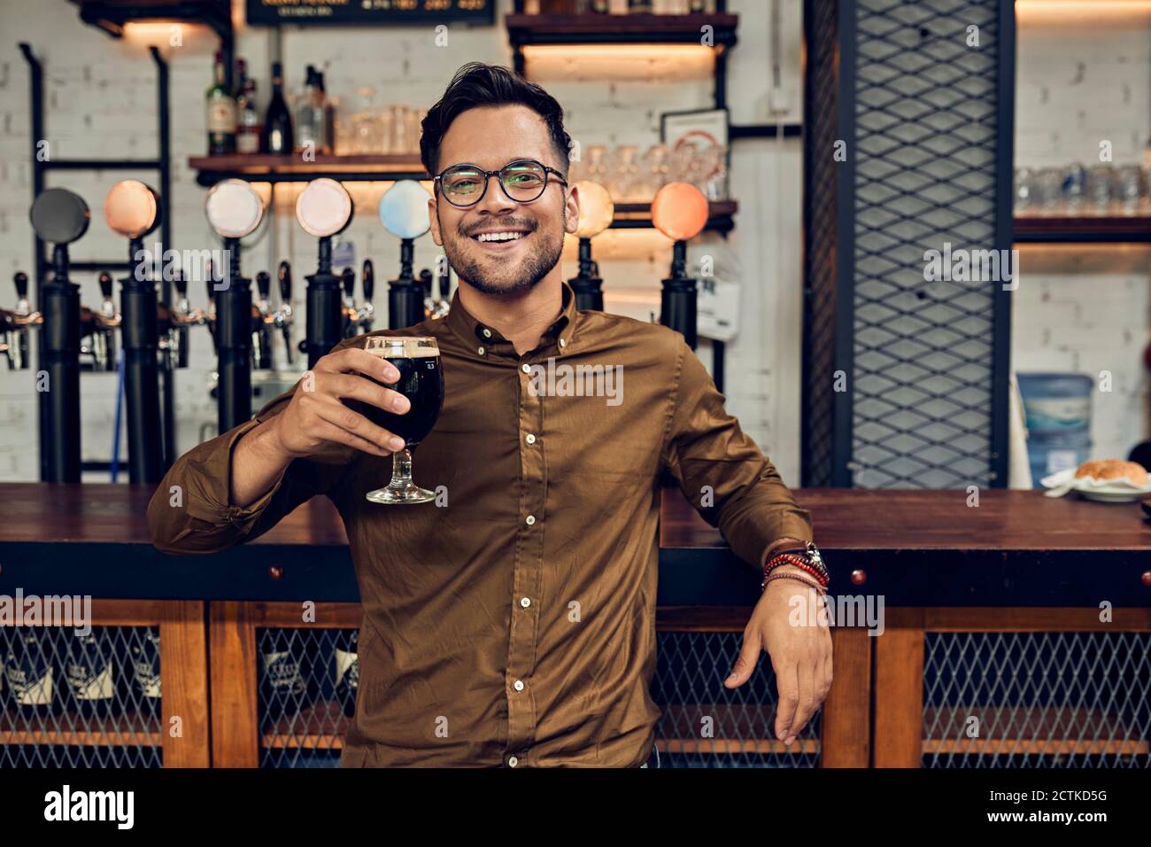 Portrait of a smiling man raising his beer glass in a pub Stock Photo