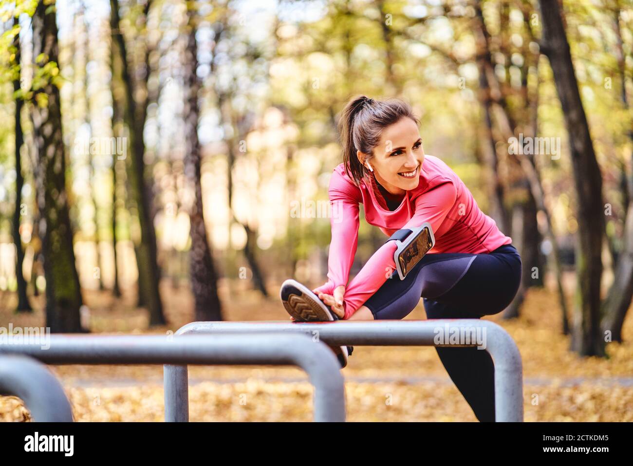 Young female jogger stretching her leg on bicycle stand in autumn forest Stock Photo