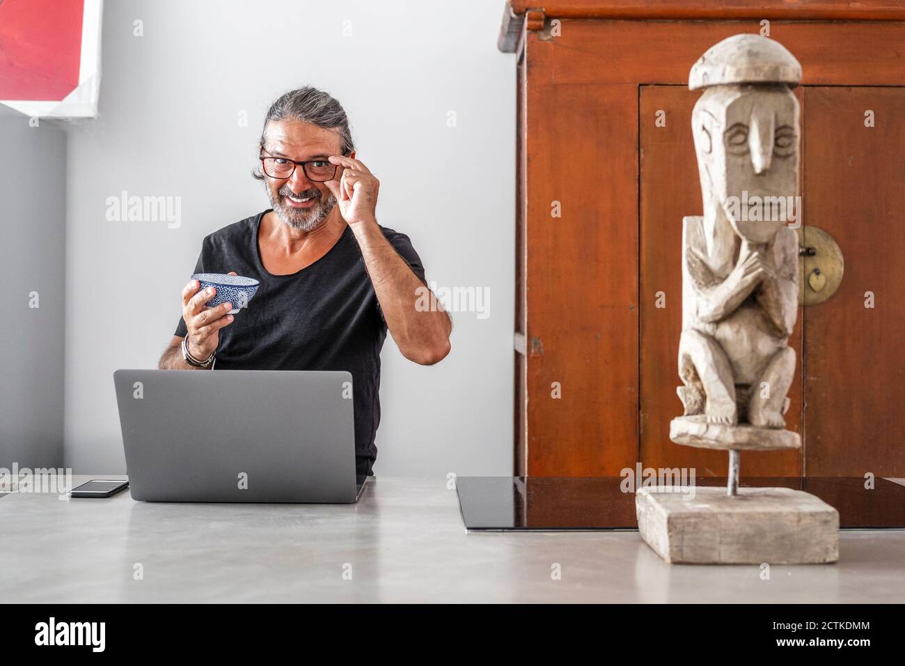 Smiling man with bowl using laptop while standing in kitchen Stock Photo