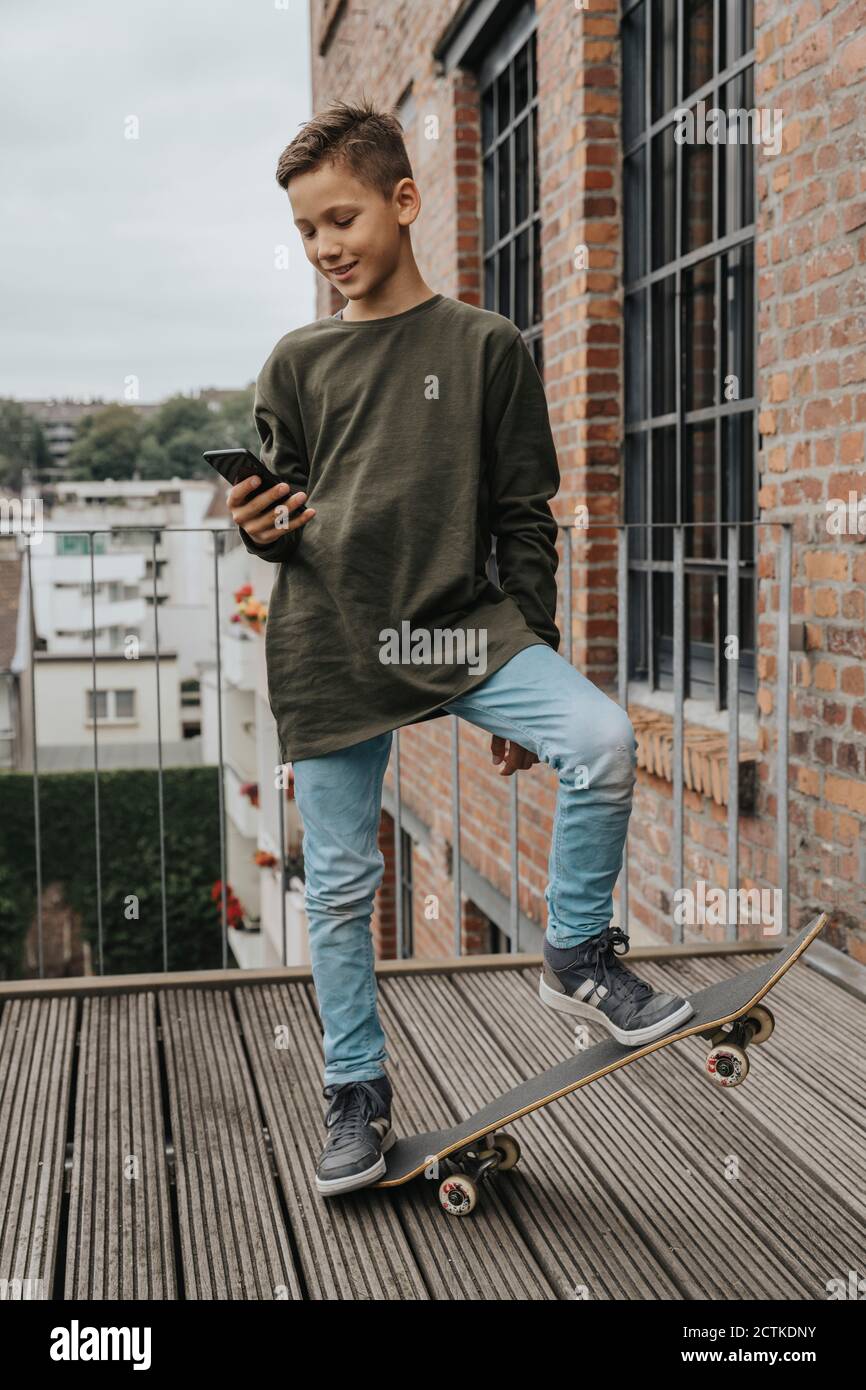 Boy using smart phone while standing with skateboard on boardwalk against railing Stock Photo