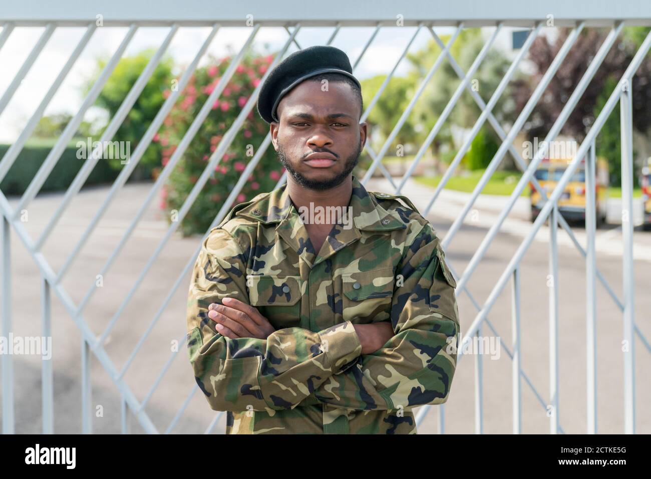 Serious army soldier with arms crossed standing against gate Stock Photo