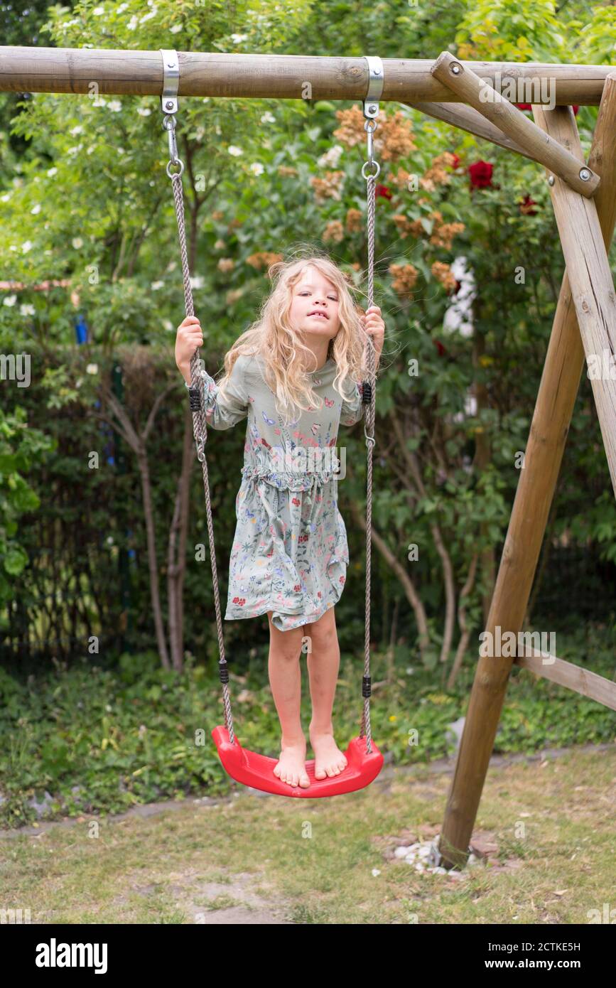 Blond girl standing on swing at back yard Stock Photo
