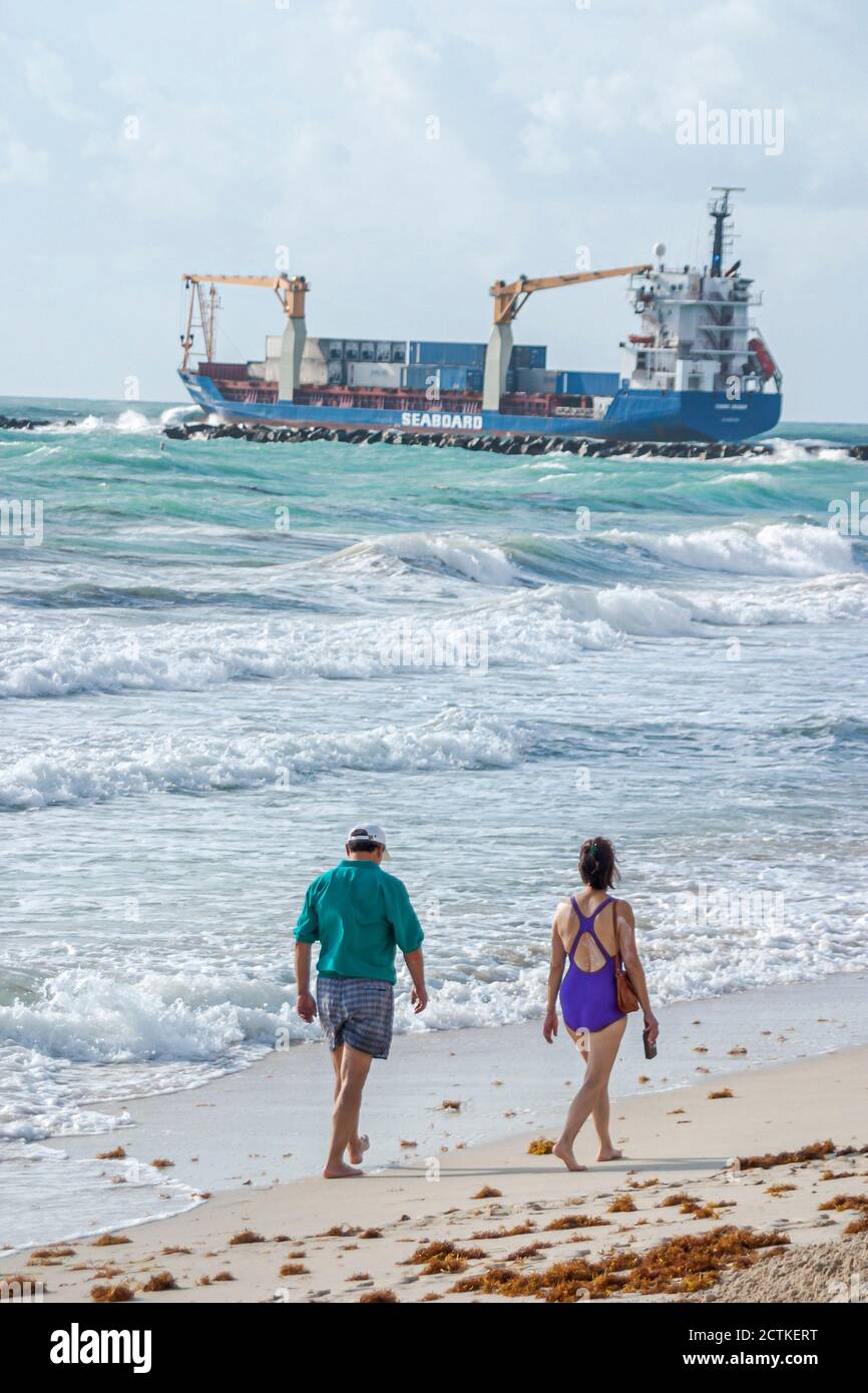 Miami Beach Florida,Atlantic Ocean shoreline coast coastline seashore,beachcombers walking man woman female couple,cargo ship boat departs Port of Mia Stock Photo