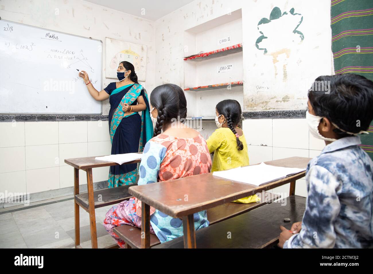 Indian teacher and students wearing face masks maintaining social distancing study in classroom back at school during covid19 pandemic. Stock Photo