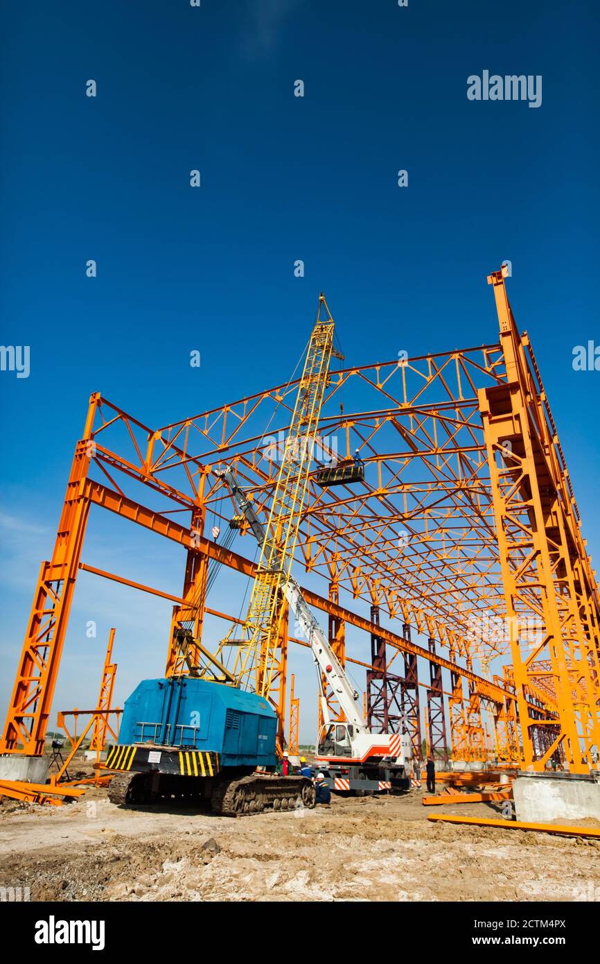 Kostanay/Kazakhstan - May 14 2012: Construction of new factory building orange steel structure. Yellow girder crane and workers in construction suspen Stock Photo