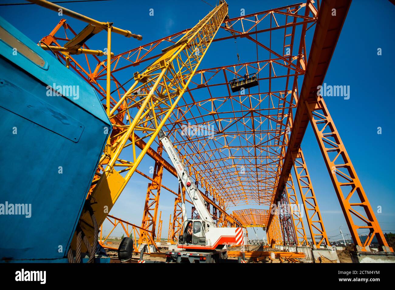Kostanay/Kazakhstan - May 14 2012: Construction of new factory building orange steel structure. Yellow girder crane and workers in construction suspen Stock Photo