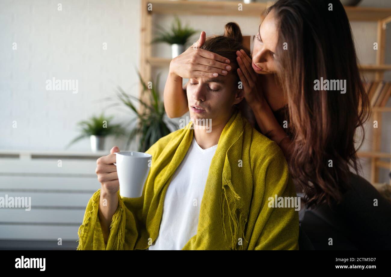 Worried woman cheks temperature of man at home. Fever, flu, illness, people concept. Stock Photo