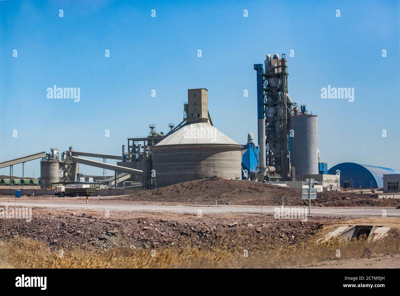 Mynaral/Kazakhstan - April 23 2012: Jambyl Cement plant tower and silos with transporter conveyors on clear blue sky and desert. Stock Photo