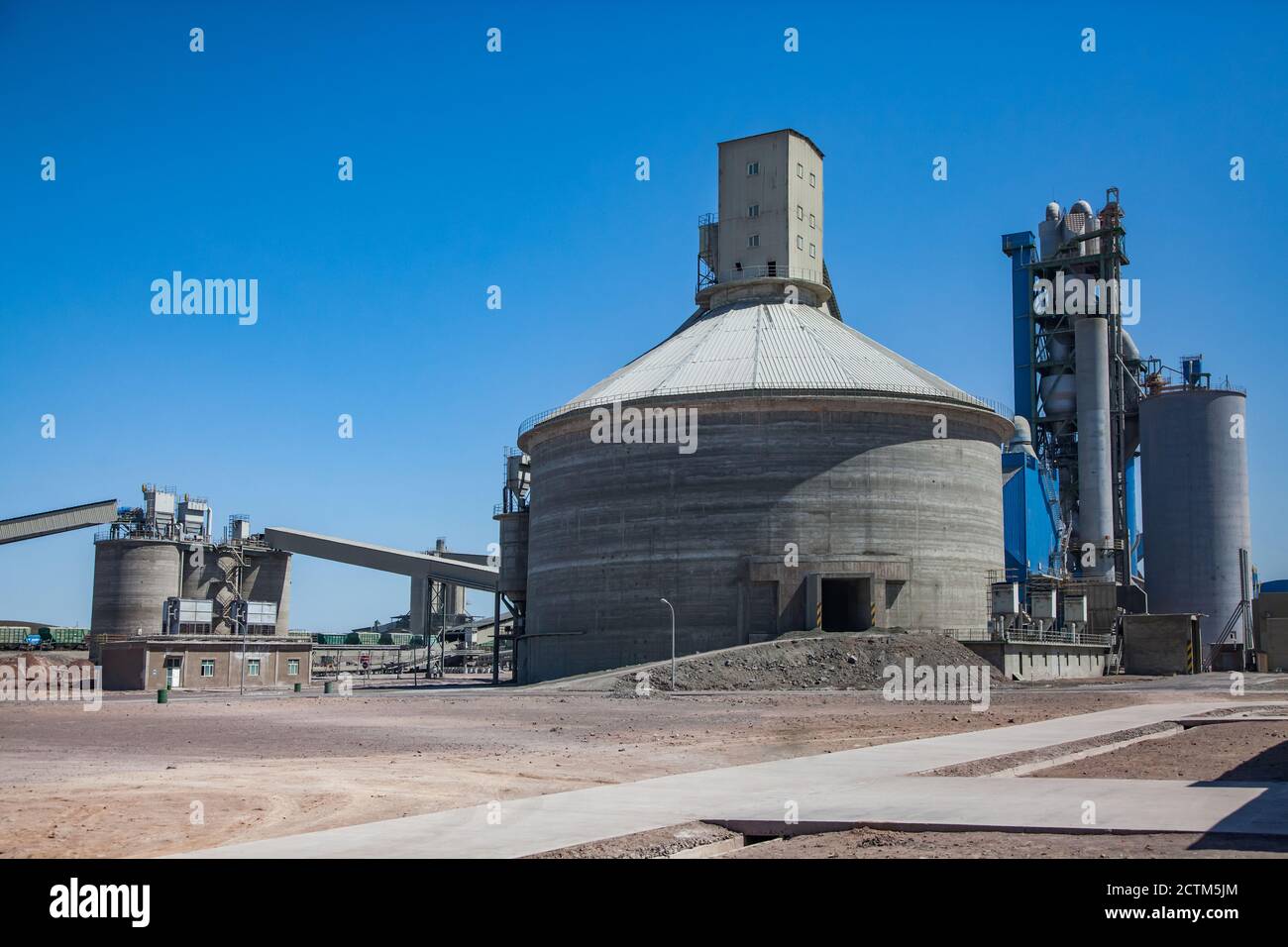 Grey concrete tower, mixing silo and conveyor (transporter) of cement plant. On clear blue sky background. Stock Photo