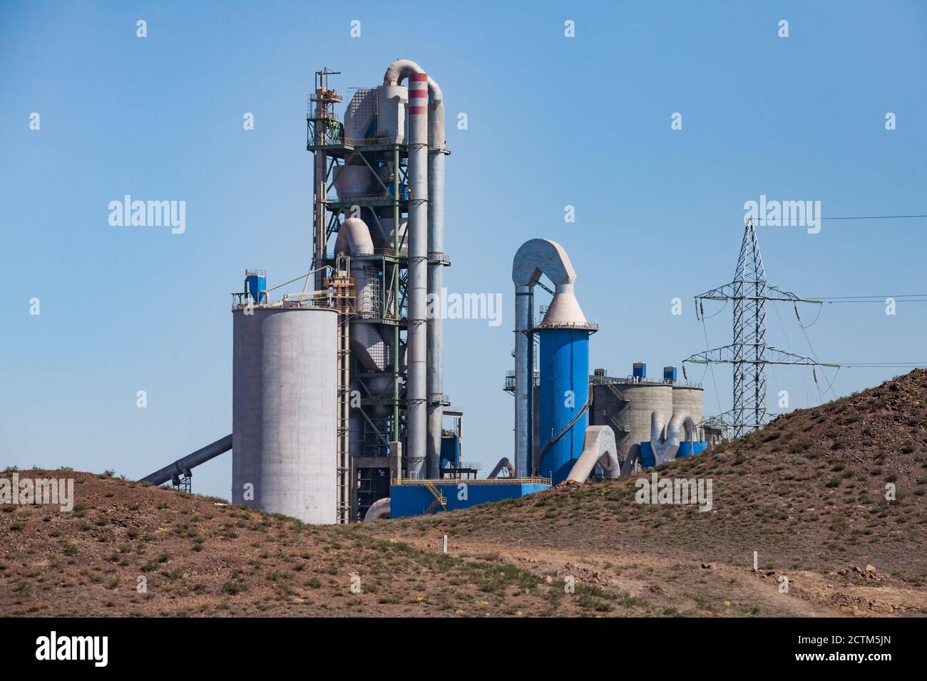 Mynaral/Kazakhstan - April 23 2012: Grey cement factory or plant Jambyl Cement tower and silos and pipes in desert on clear blue sky background. Stock Photo