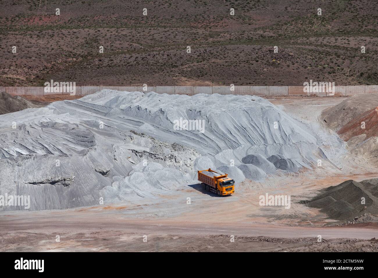 Mynaral/Kazakhstan: Grey heap of mineral clinker pellets and yellow cargo truck on Jambyl Cement plant. Stock Photo