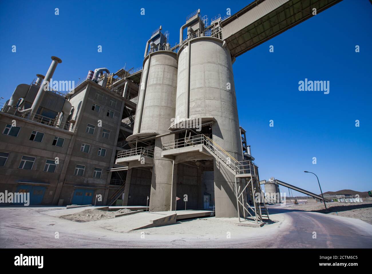 Modern cement plant in desert. Cement silos (cement tower), factory building and conveyor on blue sky. Stock Photo