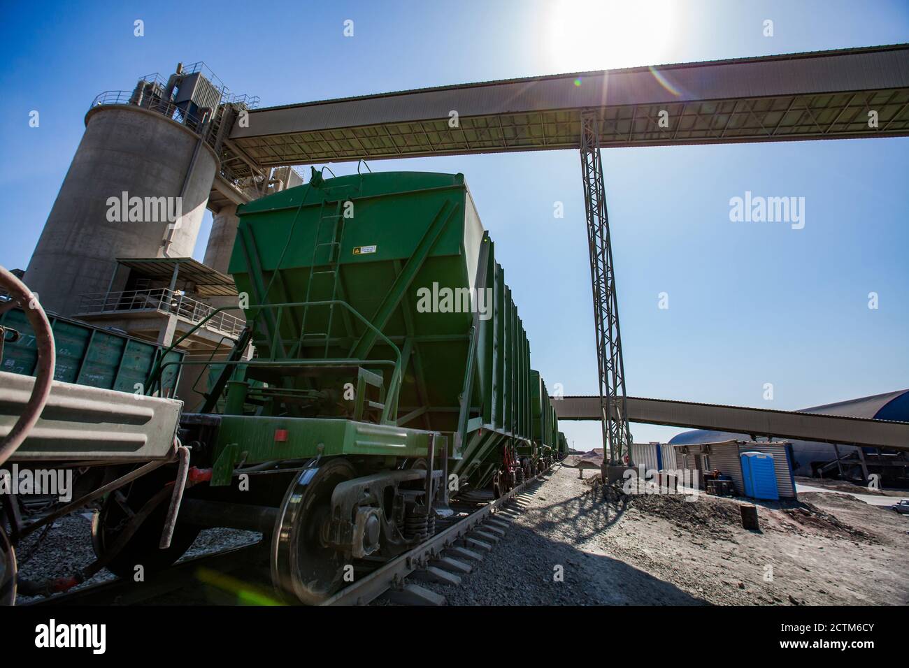 Mynaral/Kazakhstan - April 23 2012: Jambyl Cement plant. Cargo railway terminal. Rail wagons and loader conveyor on blue sky with sun. Stock Photo