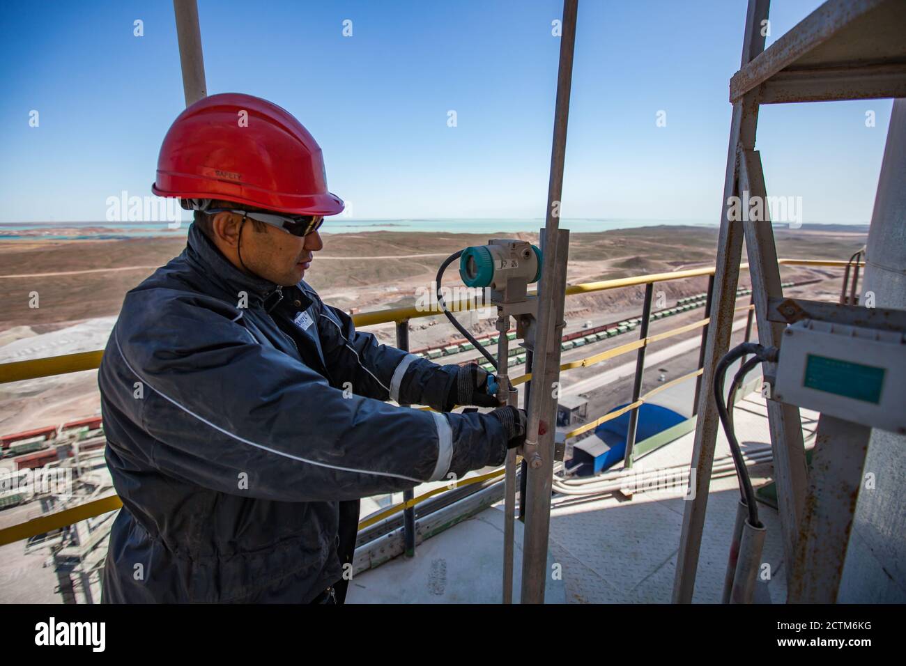 Mynaral/Kazakhstan - April 23 2012: Maintenance worker in orange helmet , dark grey work wear and protective glasses on tower (silo) of cement plant J Stock Photo