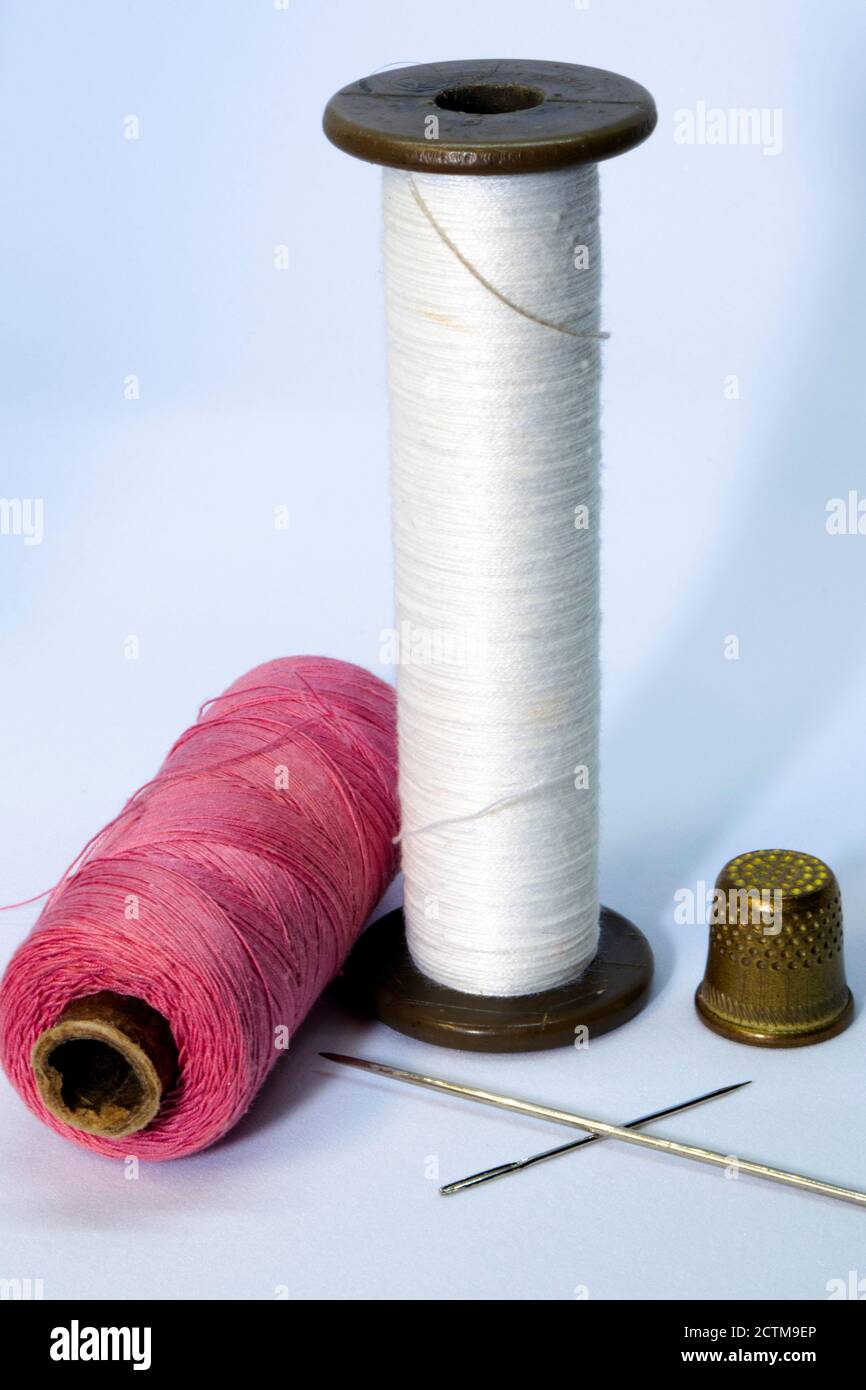 two spools of thread, two needles and a thimble on a light background Stock Photo