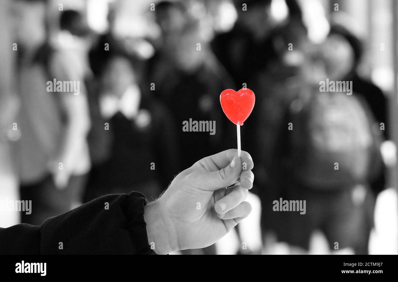 Outstretched hand offering a sign or symbol of love, care and compassion. Black and white background with isolated red colour love heart. Romantic Stock Photo