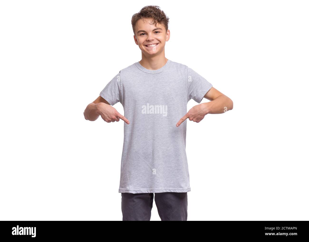 Smiling teen boy, isolated on white background. Happy child pointing fingers at blank t-shirt. Stock Photo