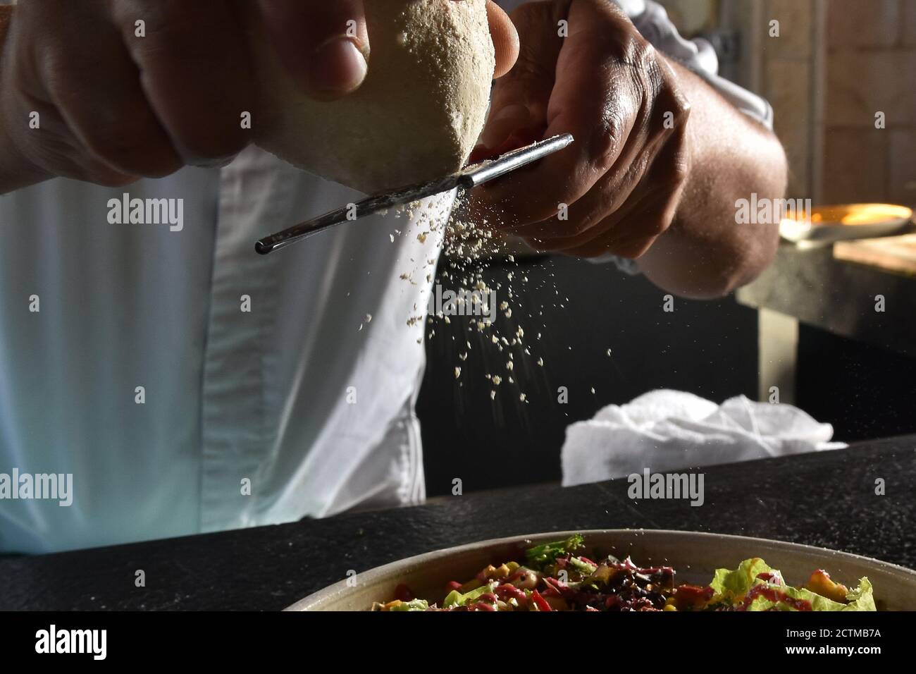 chef grates parmesan  cheese onto salad Stock Photo