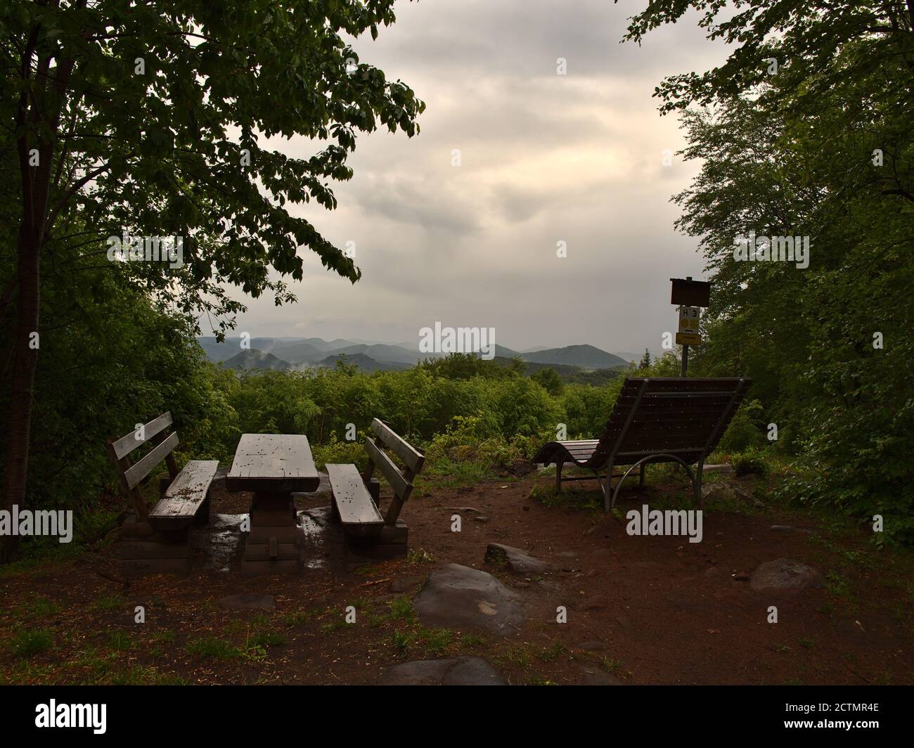 Wet picnic area with wooden benches and table after rainfall, view over Palatinate Forest, mysterious wafts of mist and cloudy weather near Dahn. Stock Photo