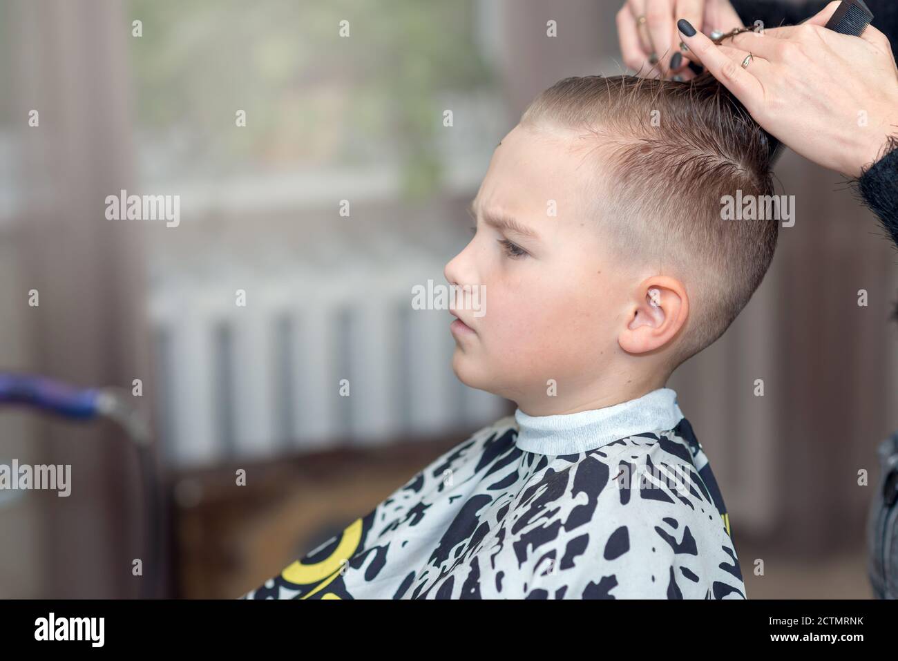 Hairdresser makes a stylish hairstyle. The woman is standing and making  haircut for blonde boy. Side view image Stock Photo - Alamy