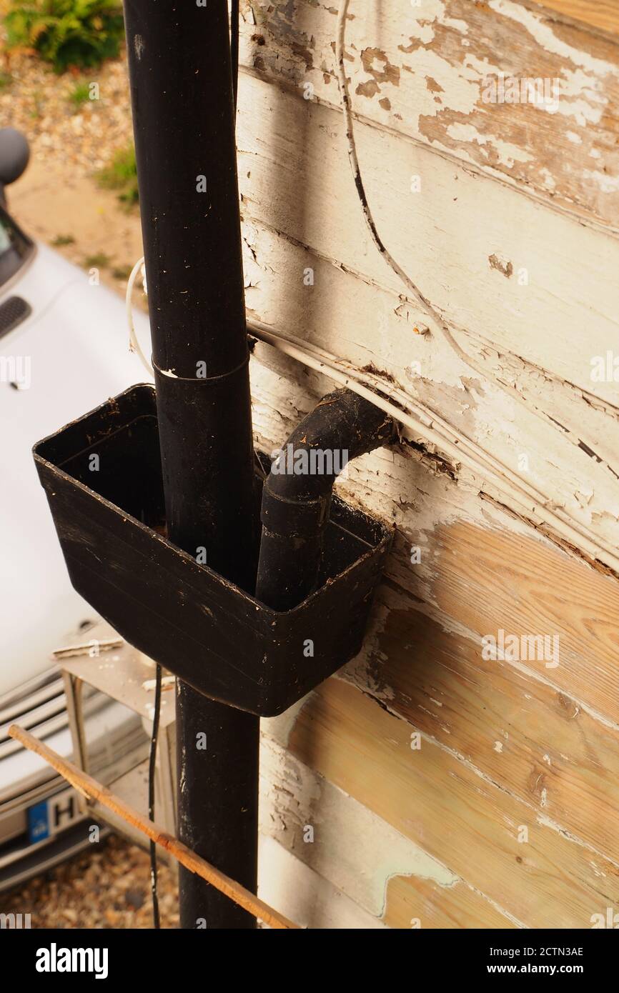 A view of a drain hopper from above joined to a timber clad exterior wall in need of repair and painting Stock Photo