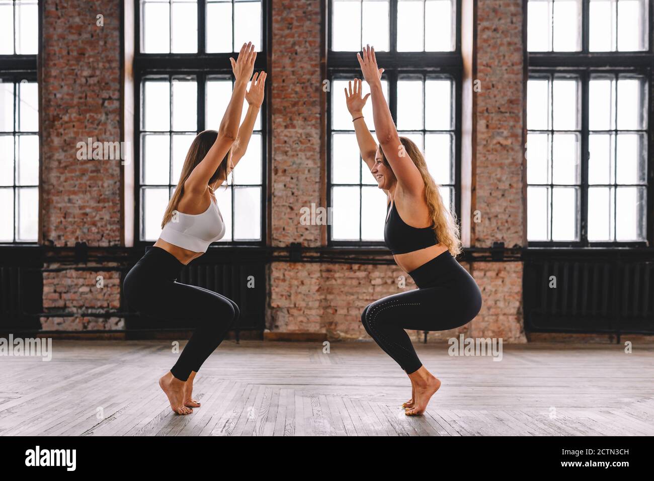 Two young women do complex of stretching yoga asanas in loft style