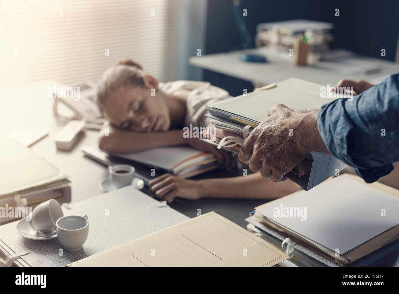 Tired lazy woman sleeping on the office desk, her boss is bringing a pile of paperwork to her desk Stock Photo