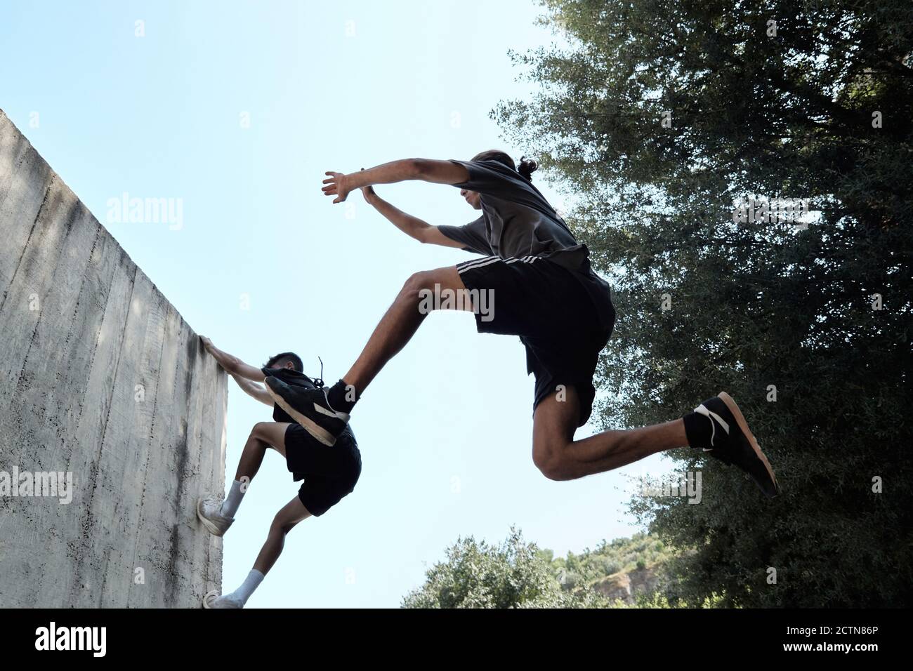 Low angle side view of unrecognizable strong men doing parkour and jumping above ground while performing dangerous trick Stock Photo