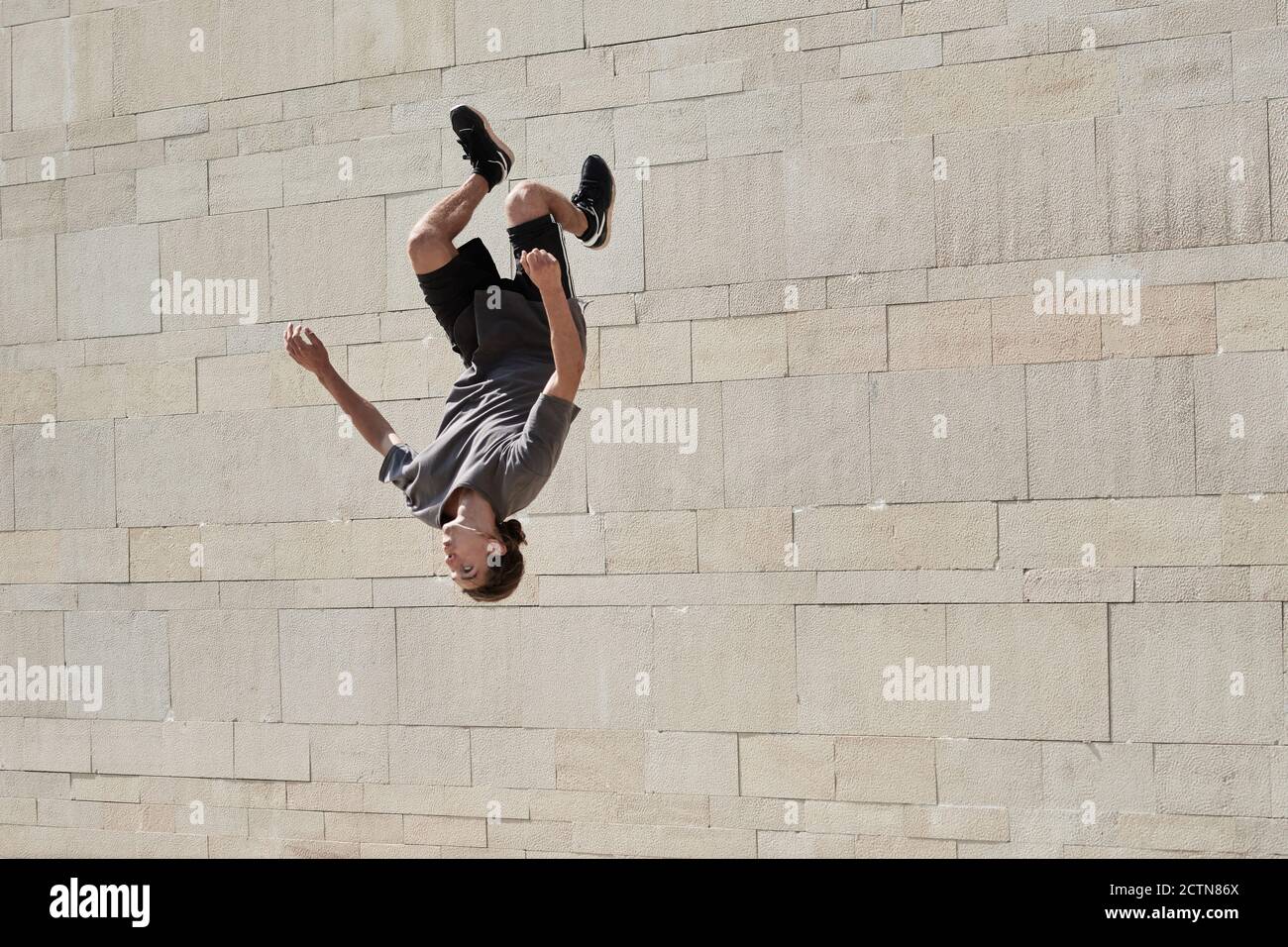 Upside down of young male doing somersault while practicing parkour in urban area in summer Stock Photo
