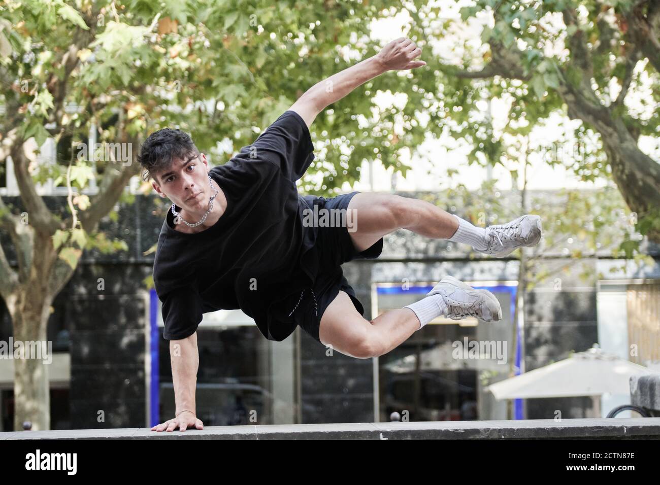 Active male in casual wear jumping over obstacle in city and performing parkour stunt while looking at camera Stock Photo