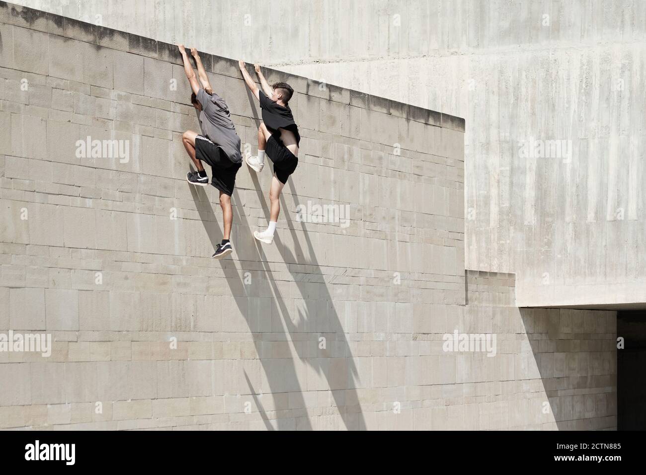 Side view of brave male friends hanging on wall of concrete building ...