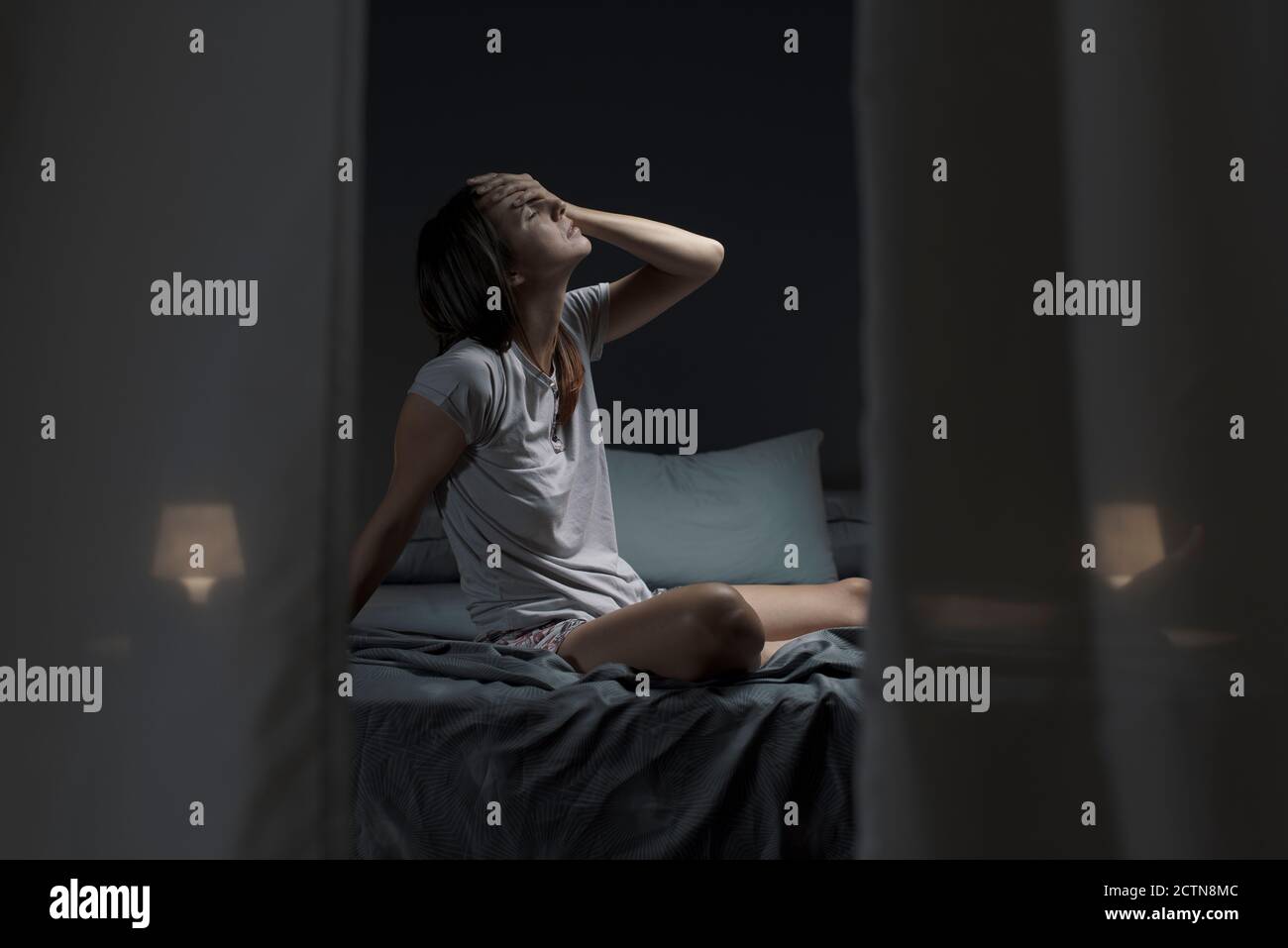 Tired woman sitting in bed at night with open window, she is suffering from the heat and she is unable to sleep Stock Photo
