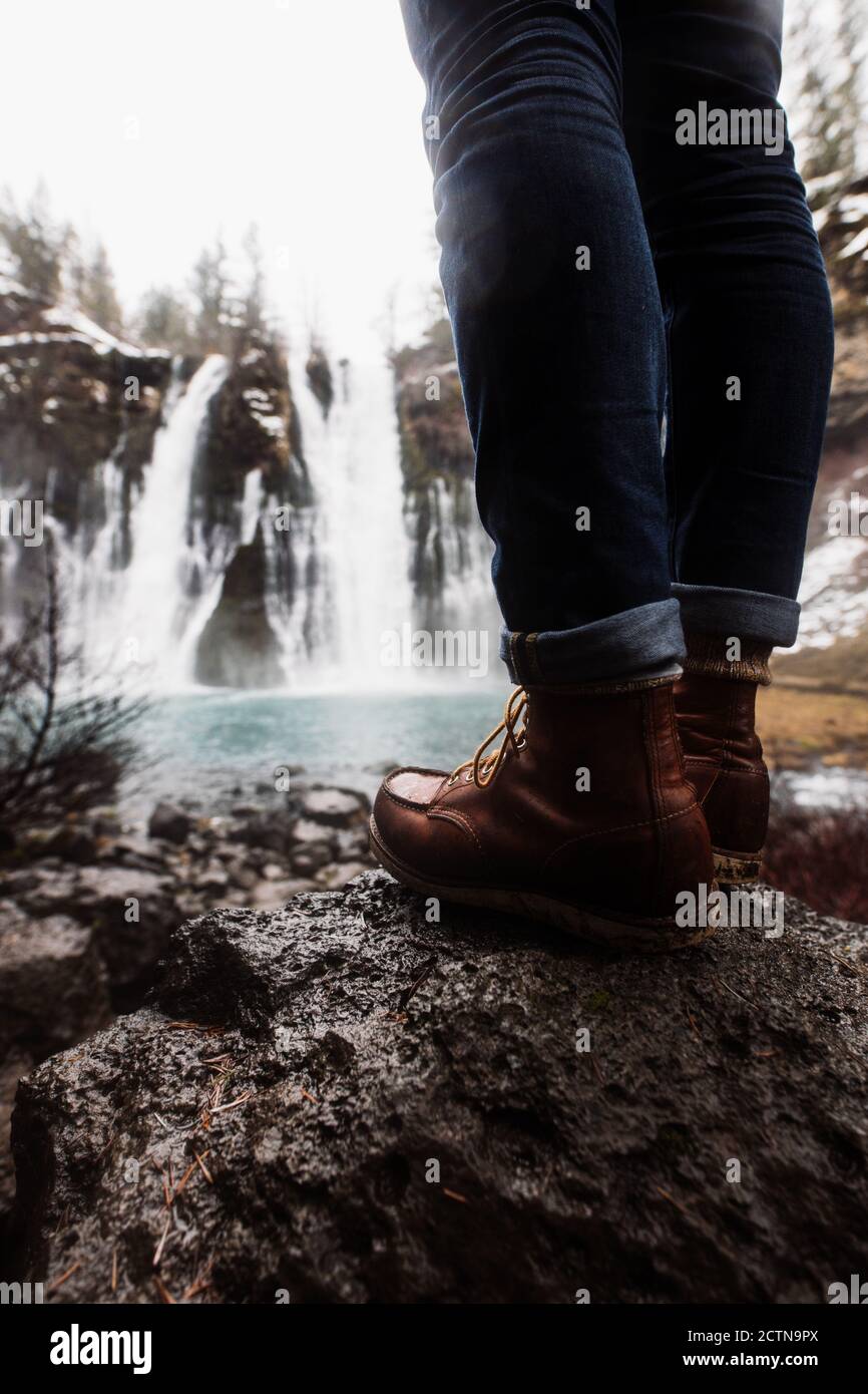 Cropped unrecognizable picturesque scenery of powerful waterfall with pool flowing among snowy forest in mountainous terrain in winter day in USA Stock Photo