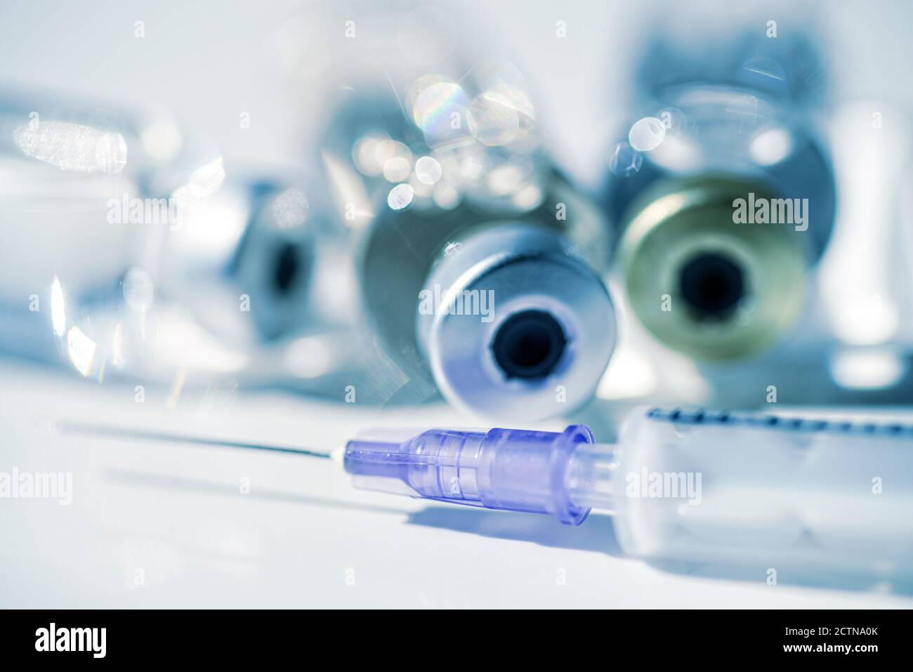 Syringe and three vials with injection material in the background Stock Photo