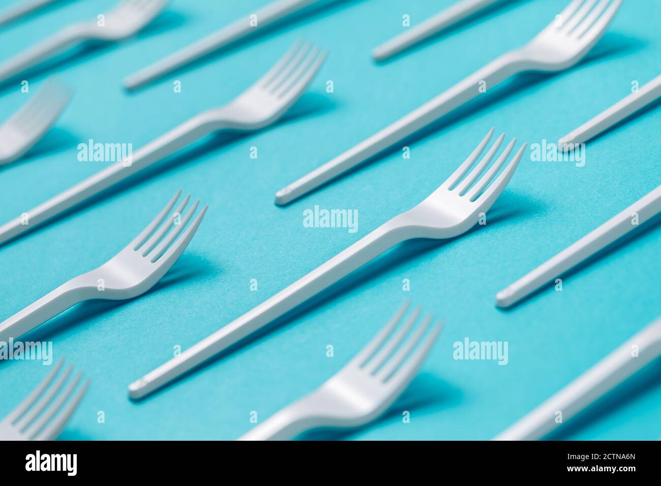 Top view flat lay composition of disposable white plastic forks for takeaway food arranged on blue background Stock Photo