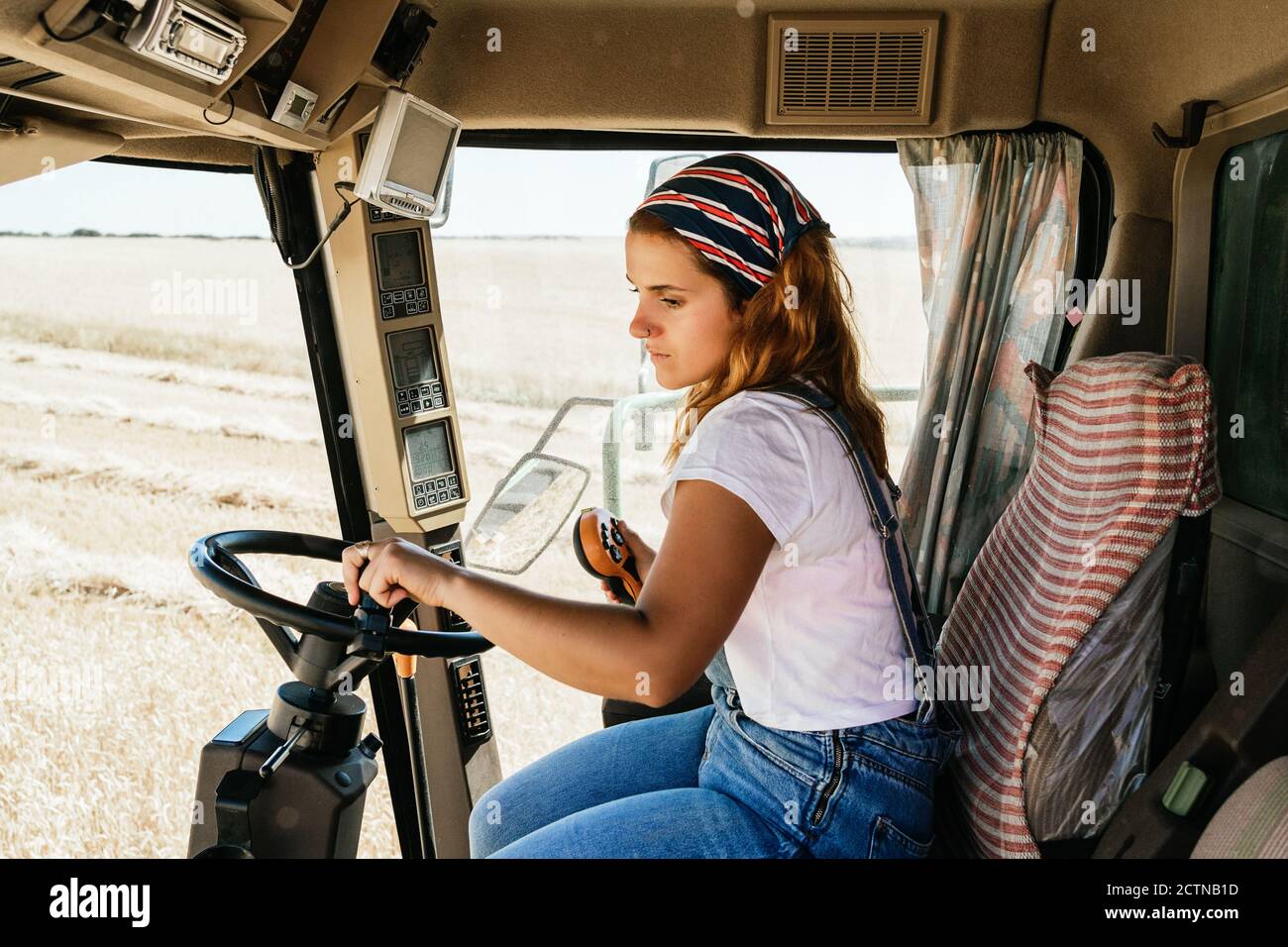 Side view of serious female farmer operating combine harvester and collecting wheat in field in rural area Stock Photo