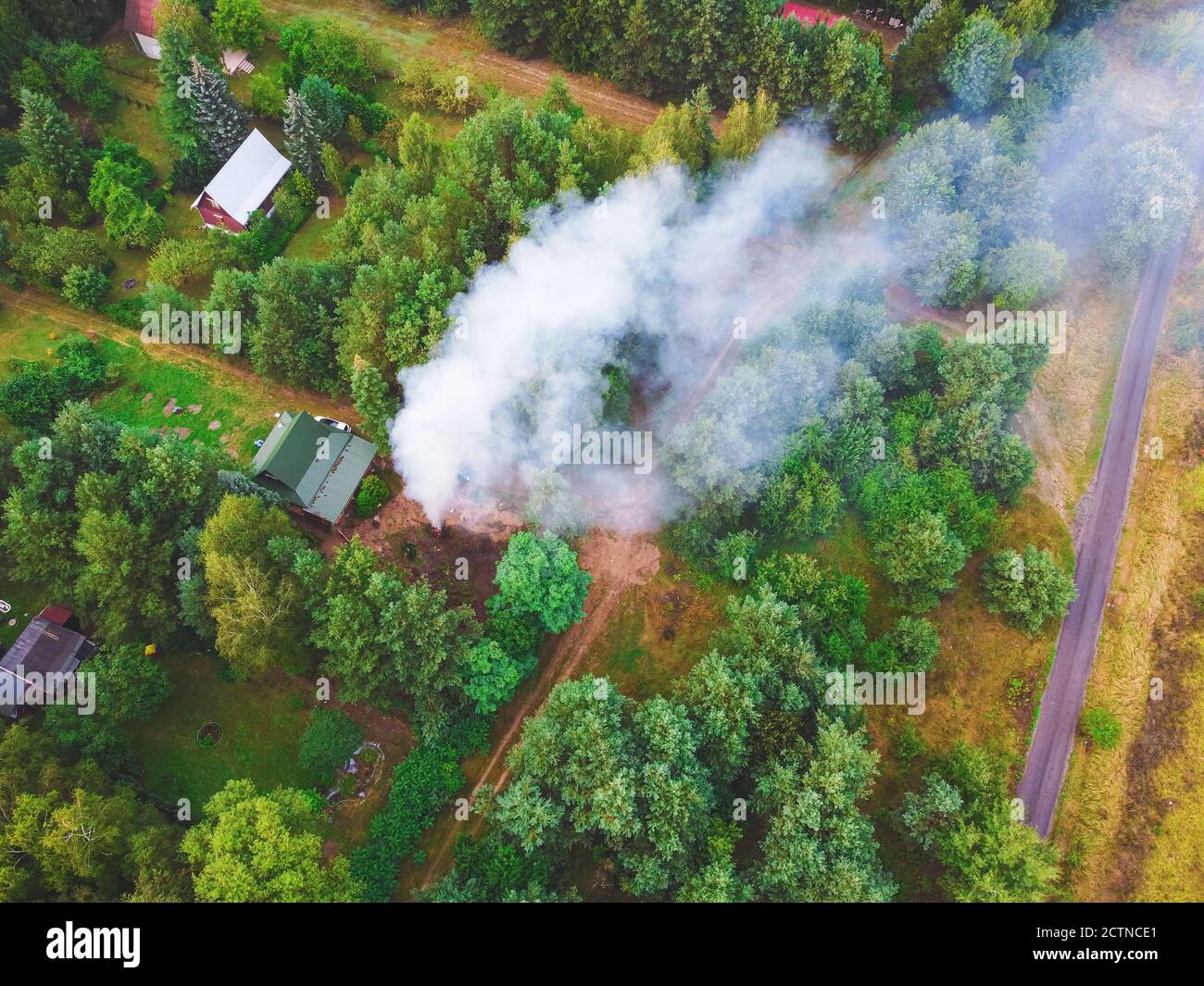 Smoke from the fire over cottages in the forest. Drone, aerial View. Stock Photo