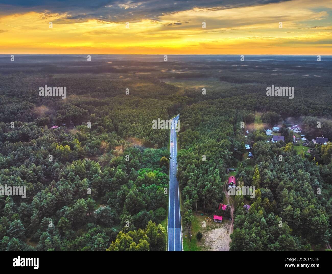 High up view of the road disappeared into the forest during sunset. Drone, aerial view. Stock Photo