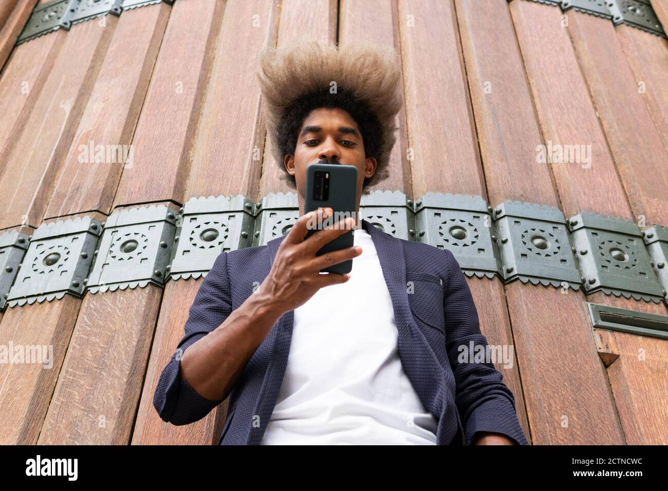 From below of an african man in suit using his mobile phone in front of a wooden wall Stock Photo