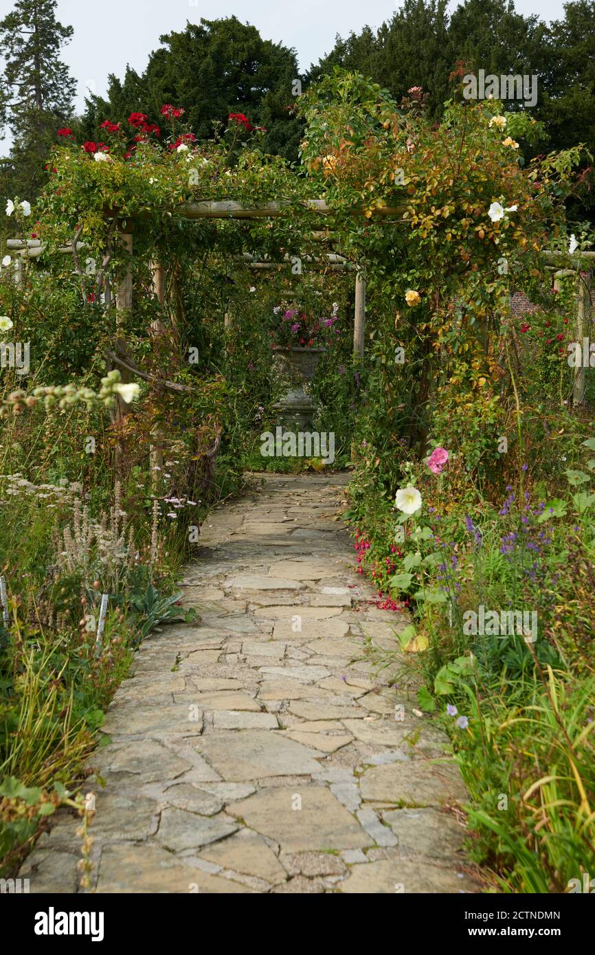 A path made of crazy paving leading through a rose arch garden in ...