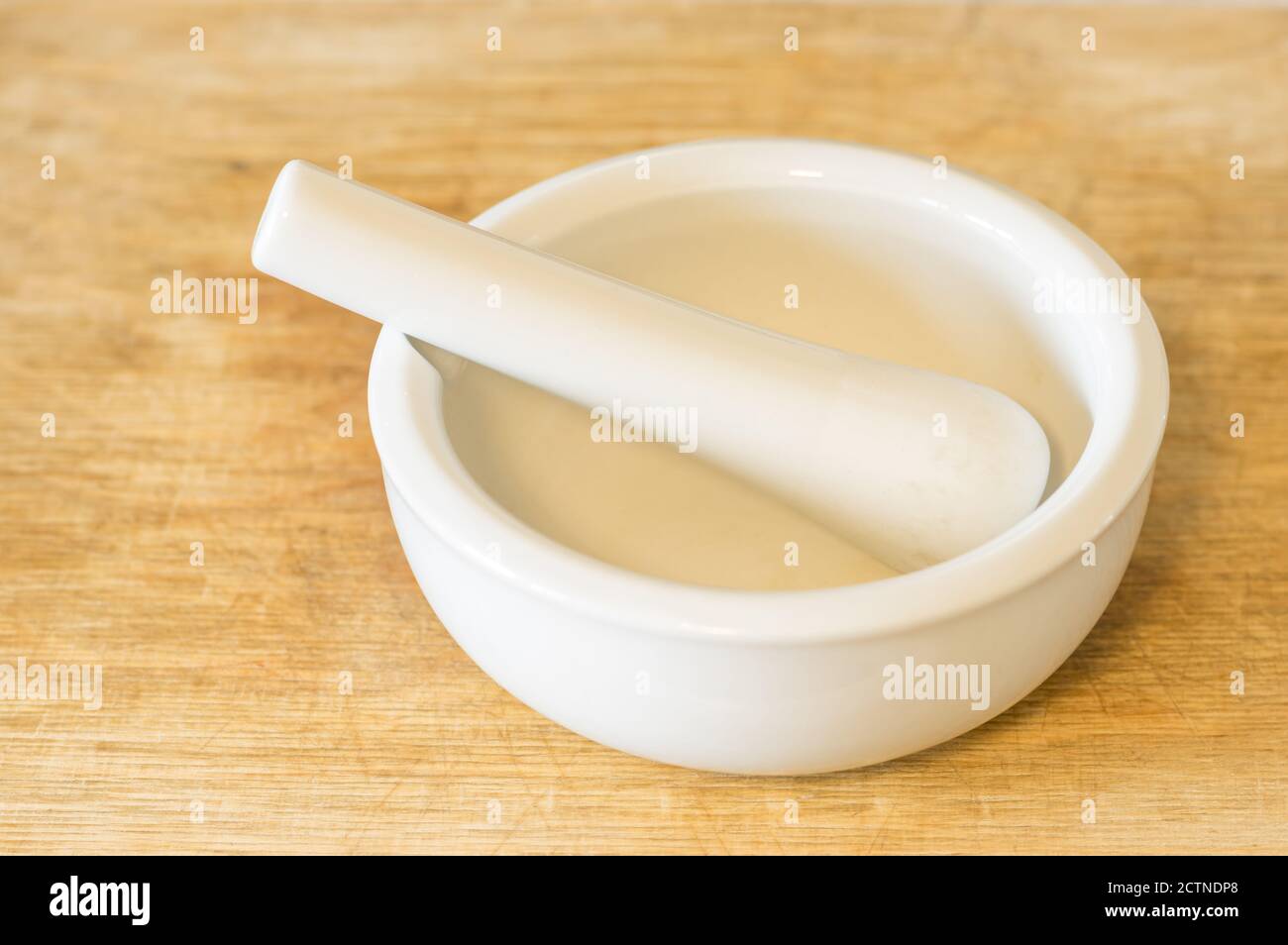 White ceramic mortar lying on a wooden cutting board Stock Photo