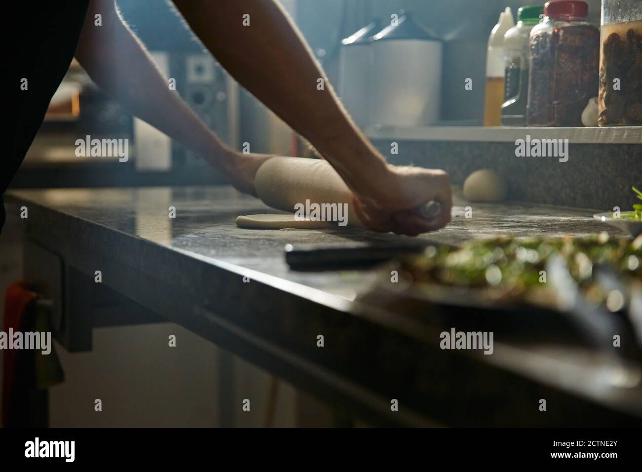 Cropped anonymous man using rolling pin to stretch fresh dough on on marble counter table while preparing pizza in kitchen Stock Photo