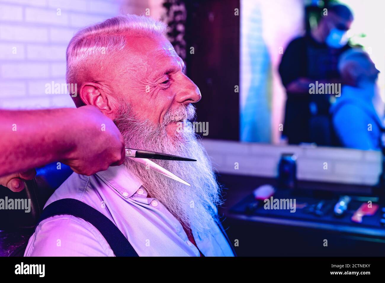 Male hairdresser cutting hair to hipster senior client - Side view of young hairstylist working in barbershop - haircut profession concept Stock Photo