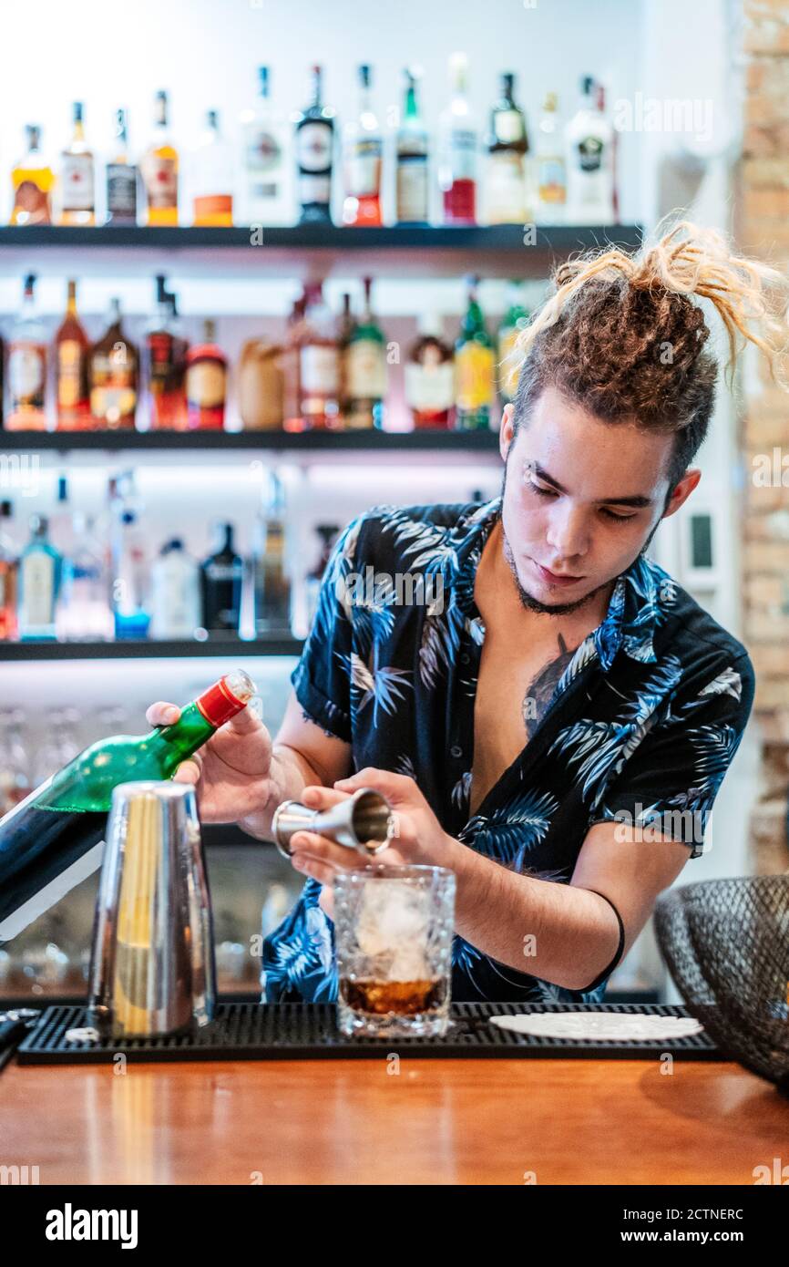Smiling male bartender wiping a glass and looking away. Barista in