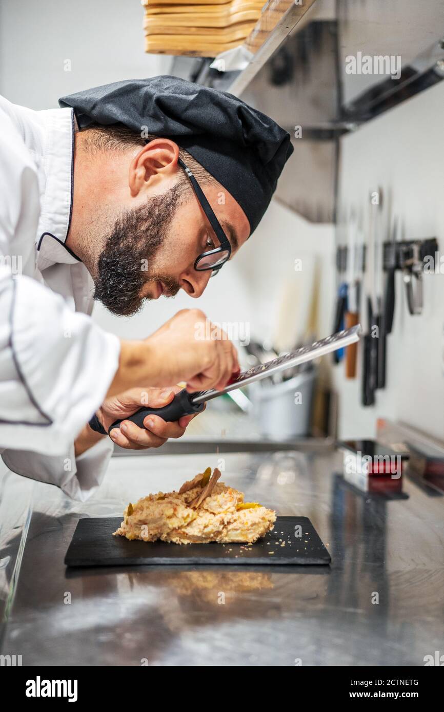 Side view of busy male cook using grater and garnishing sweet dessert placed on slate board in kitchen Stock Photo