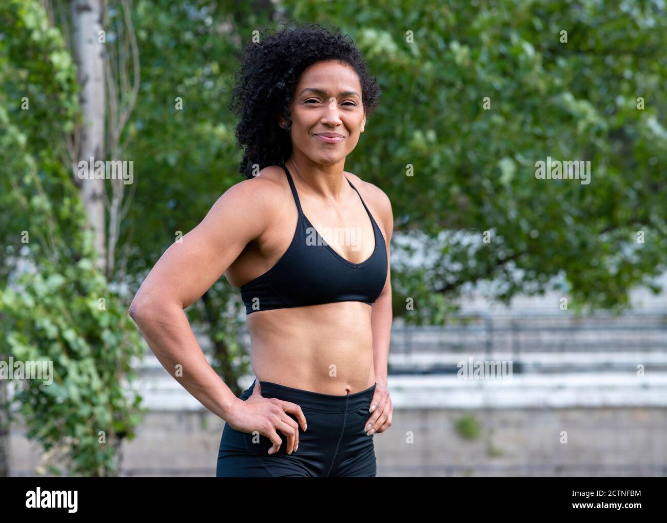 Confident African American athletic female with muscular body standing with  hands on waist in city during training and looking at camera Stock Photo -  Alamy