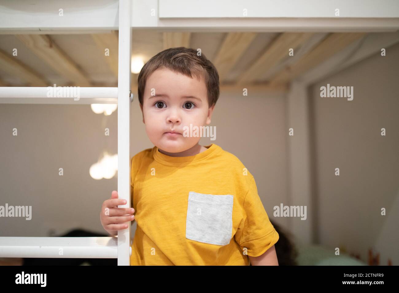 Cute little boy in pajama standing on bed in room with illuminated garland Stock Photo
